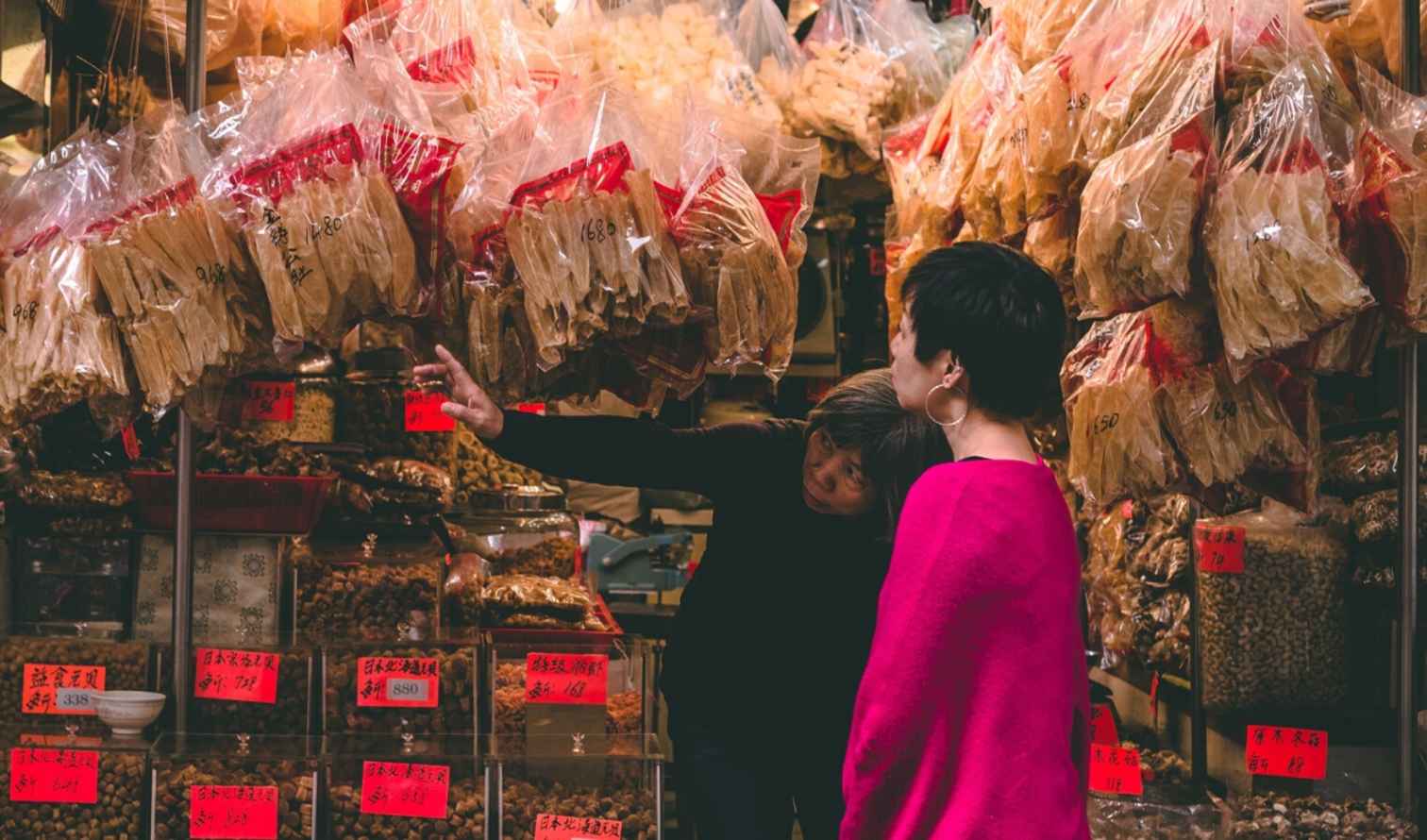 Two people examining dried goods at a market stall in Hong Kong.