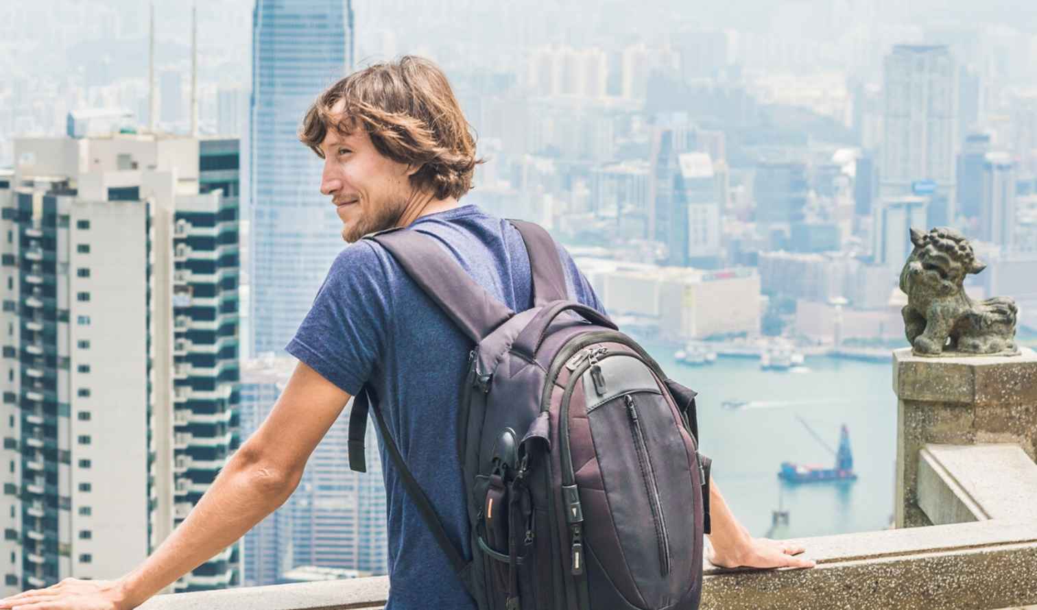 Man with backpack overlooking Hong Kong skyline from Victoria Peak.