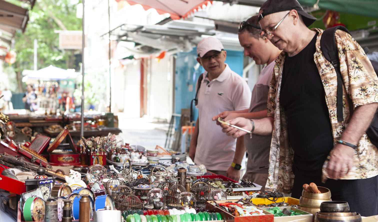 Three men browsing trinkets at a Hong Kong street market.