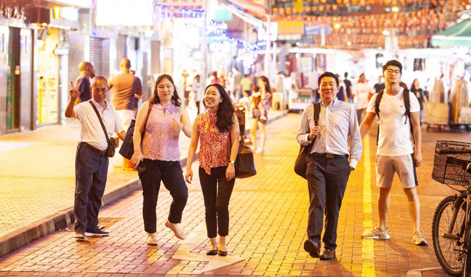People walking on a busy street with orange lanterns overhead in Hong Kong 