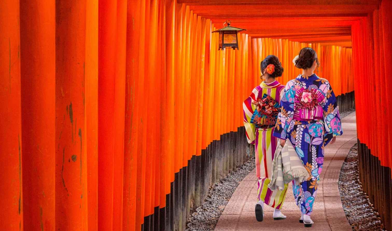 Two people wearing kimonos walk through the Fushimi Inari Shrine torii gates in Kyoto