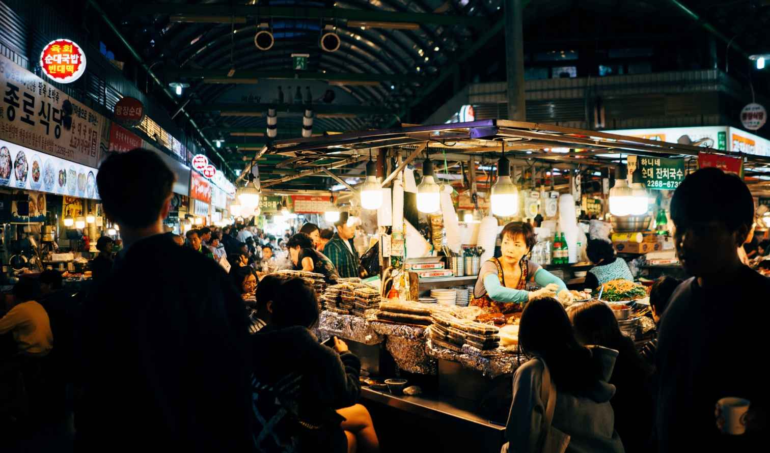 A busy food stall inside Gwangjang Market, Seoul, with many people dining.