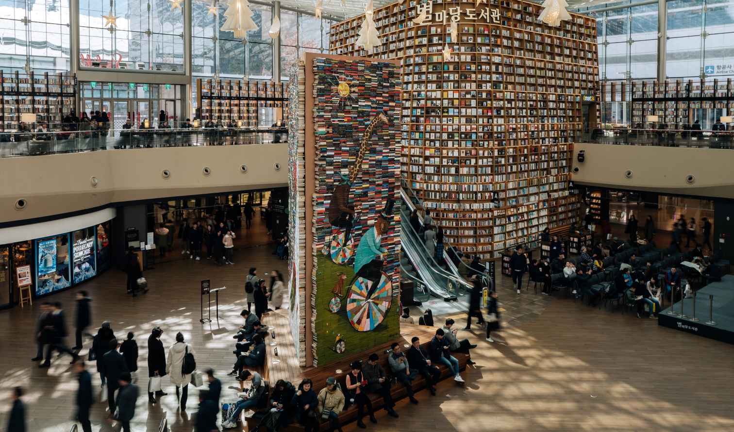People walking in Starfield Library with a large bookshelf and mural wall in Seoul.