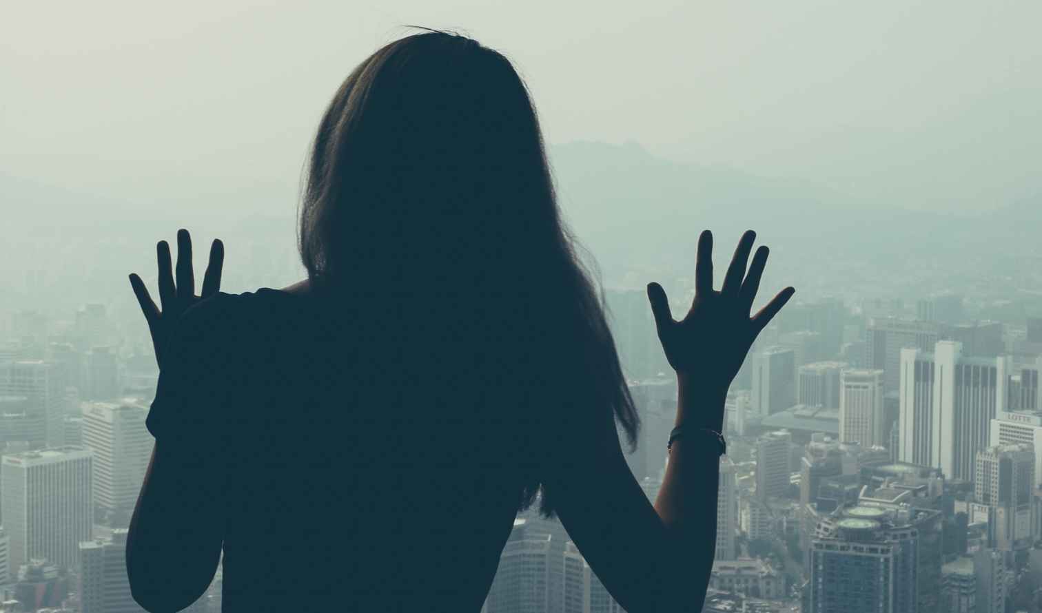 Silhouette of a woman looking over a city from a high viewpoint in Seoul.