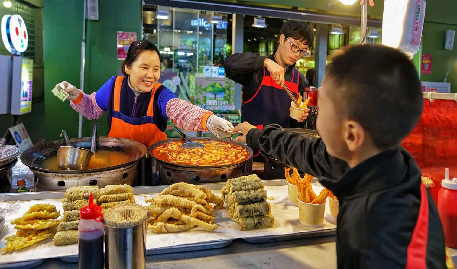 A street vendor serving food to a child in a market in Seoul.
