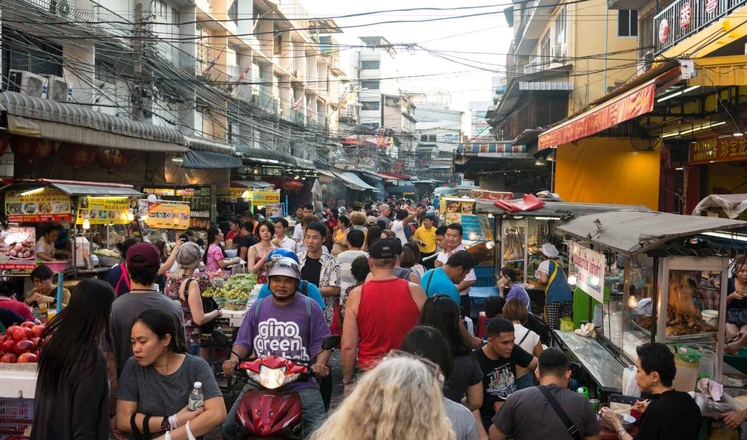 People walking through a busy market in Bangkok, Thailand, with various vendors.