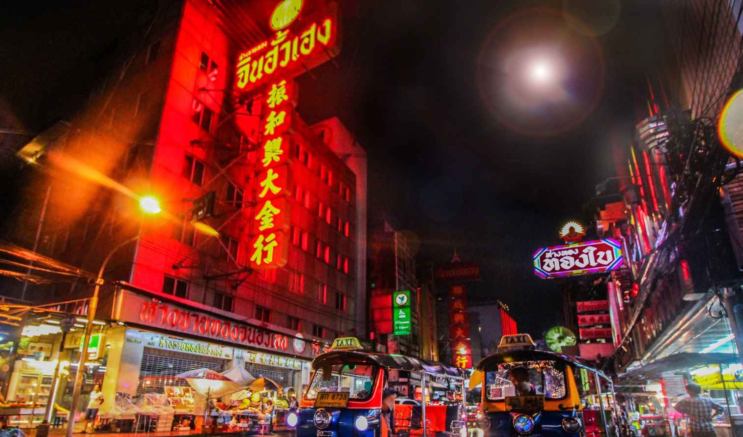 Tuk-tuks on a street in Yaowarat, Bangkok with neon lights.