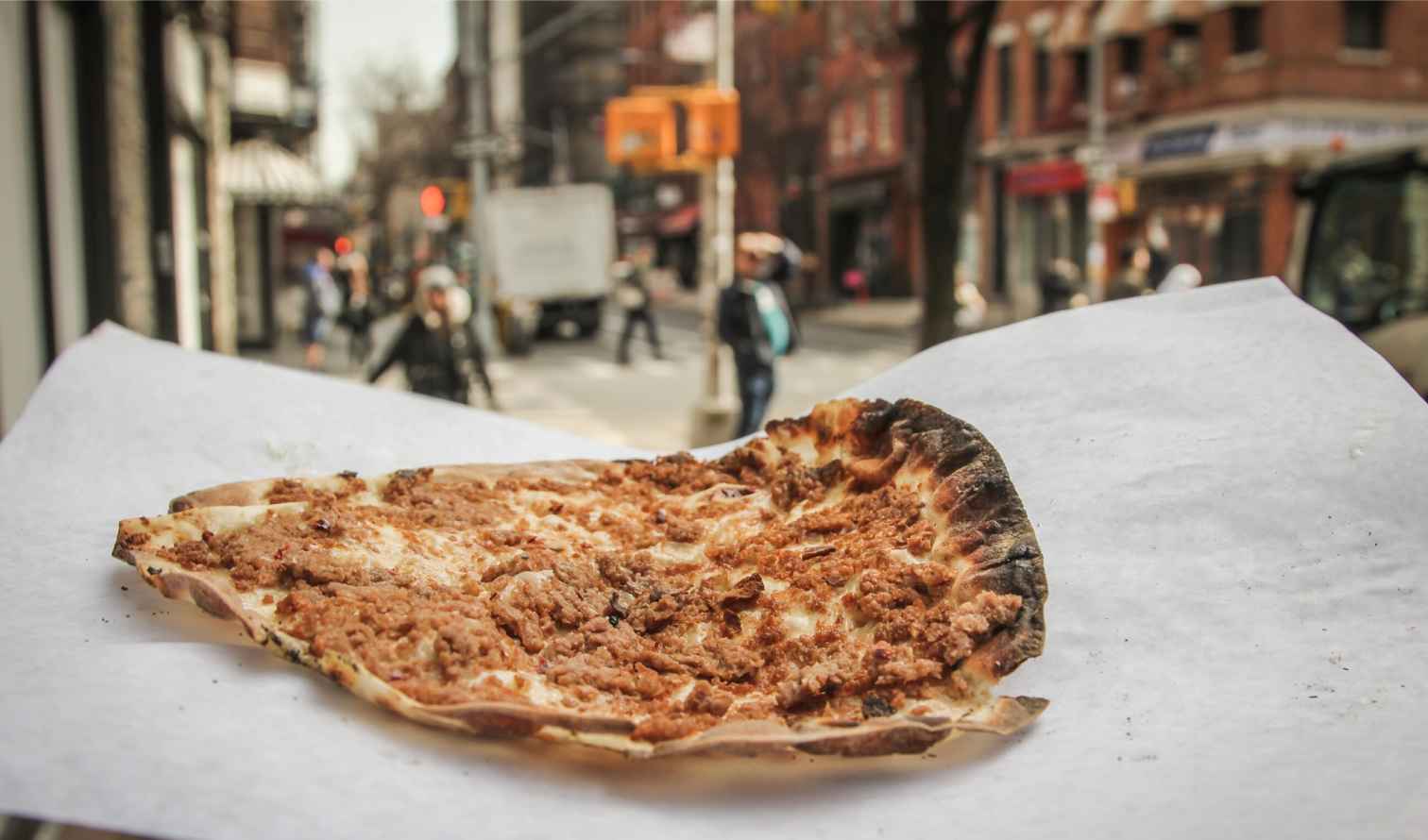 A slice of pizza on a paper plate held on a New York street.