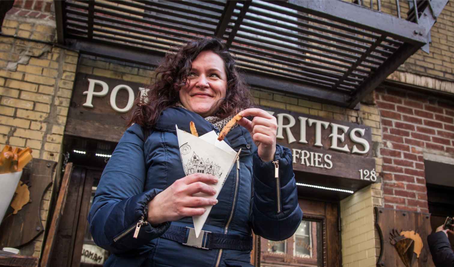 Woman holding fries outside Pommes Frites store at 128 Macdougal Street in New York