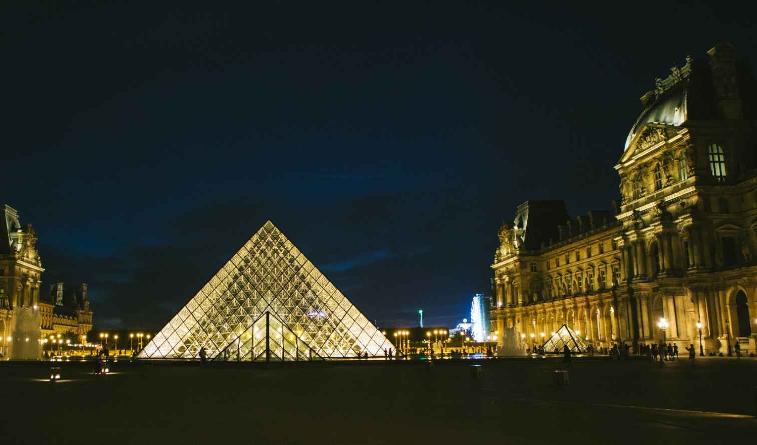 The Louvre Museum with illuminated pyramid at night in Paris, France.