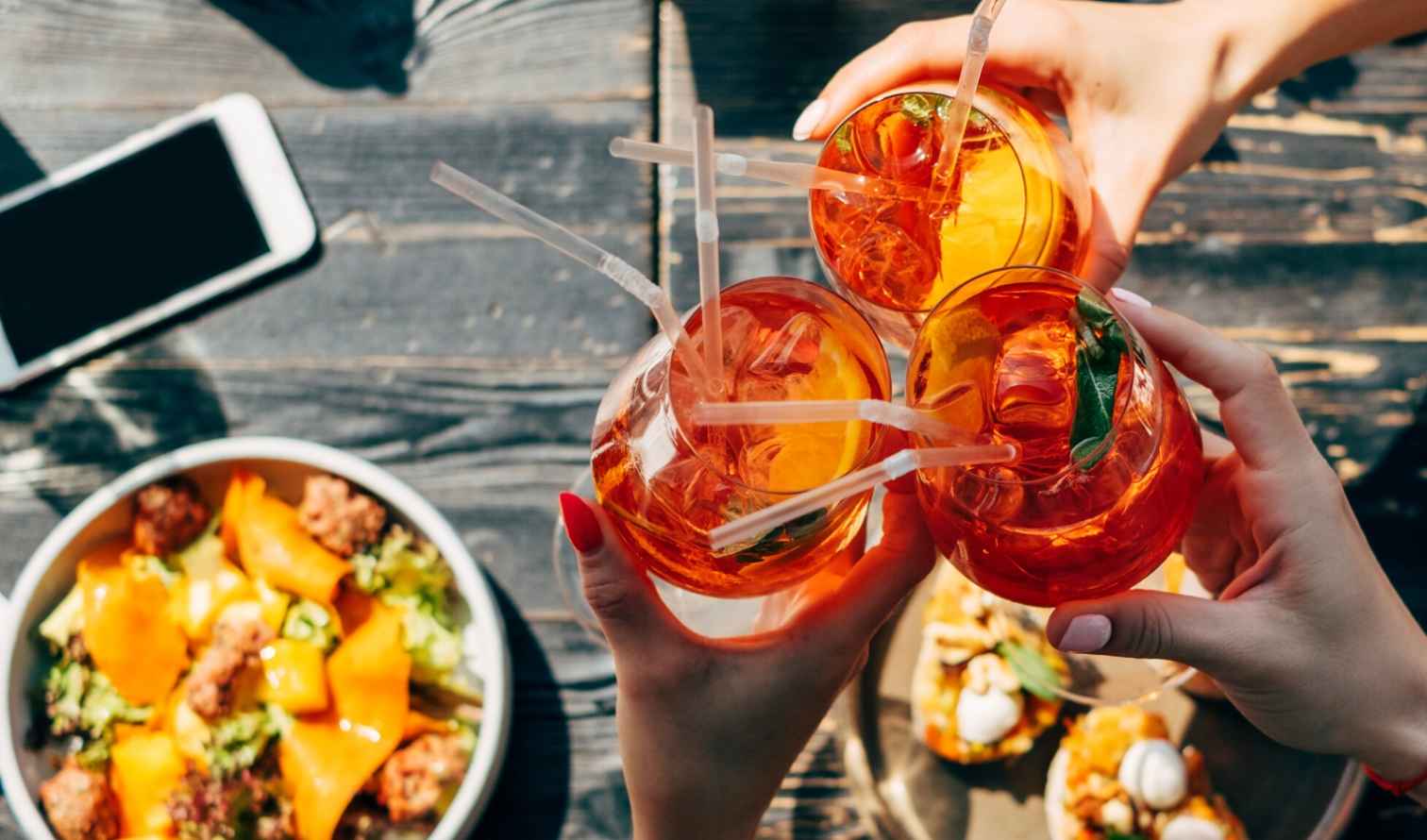 Hands with manicured nails holding three Aperol Spritz glasses in Milan