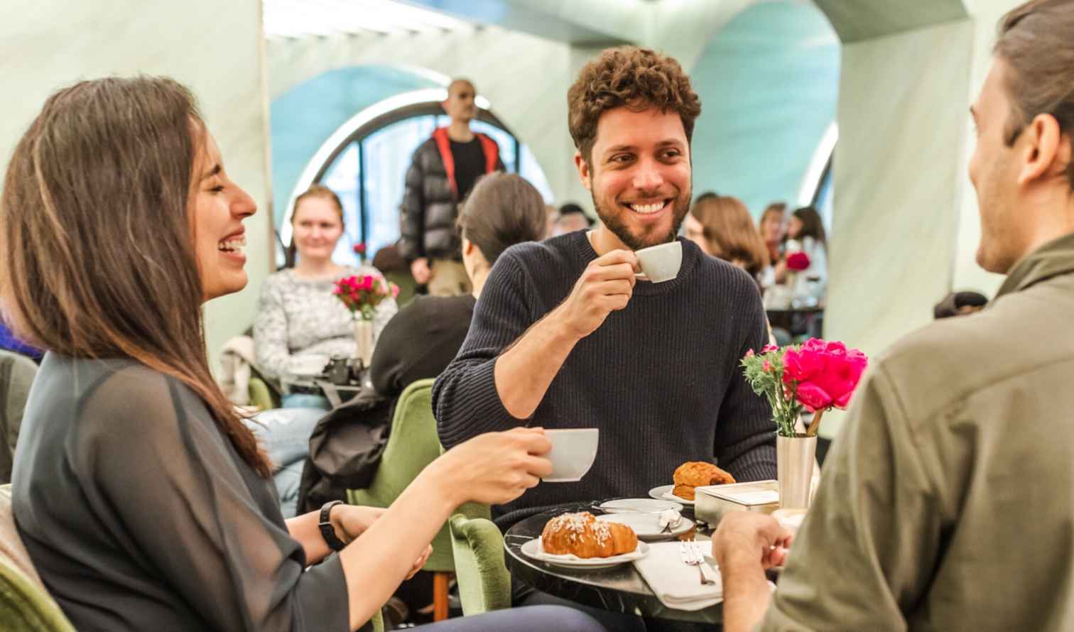 Three people sitting at a cafe table, one holding a coffee cup in Milan