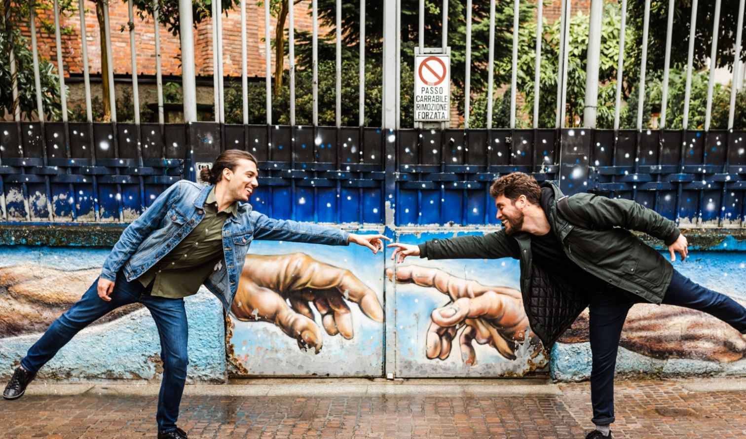 Two men pose playfully in front of street art in Milan.