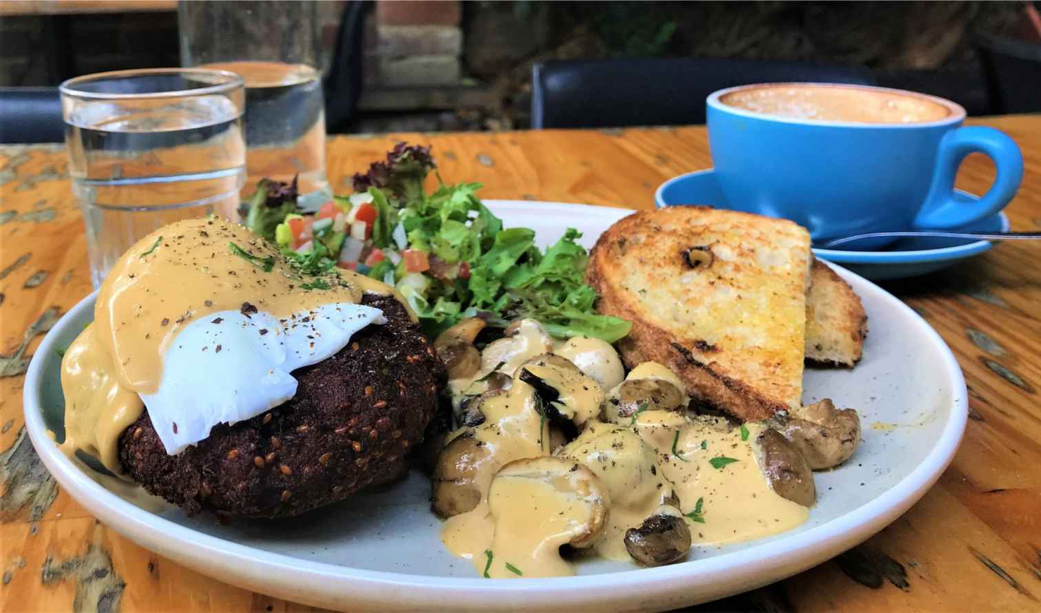 Brunch plate with poached egg, mushrooms, salad, and toast on a wooden table in Sydney