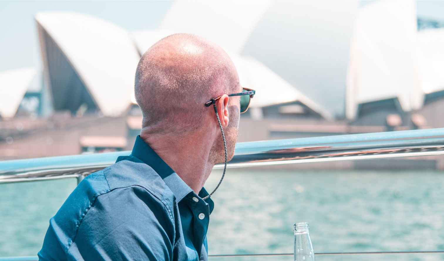 Man in sunglasses viewing the Sydney Opera House from a boat.