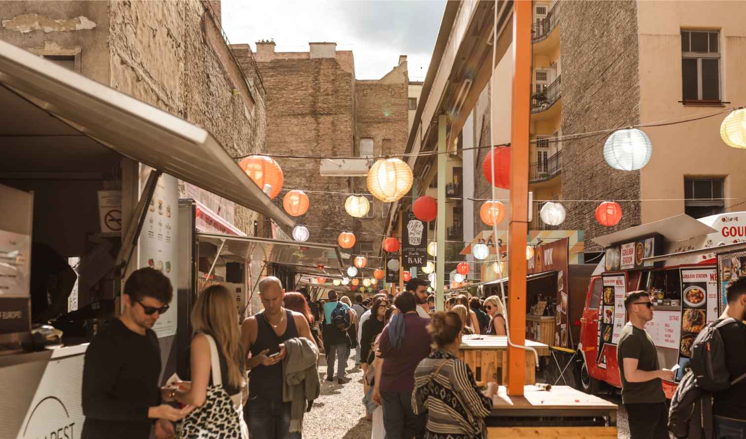 Outdoor market scene in Gozsdu Courtyard, Budapest, with people and food stalls.