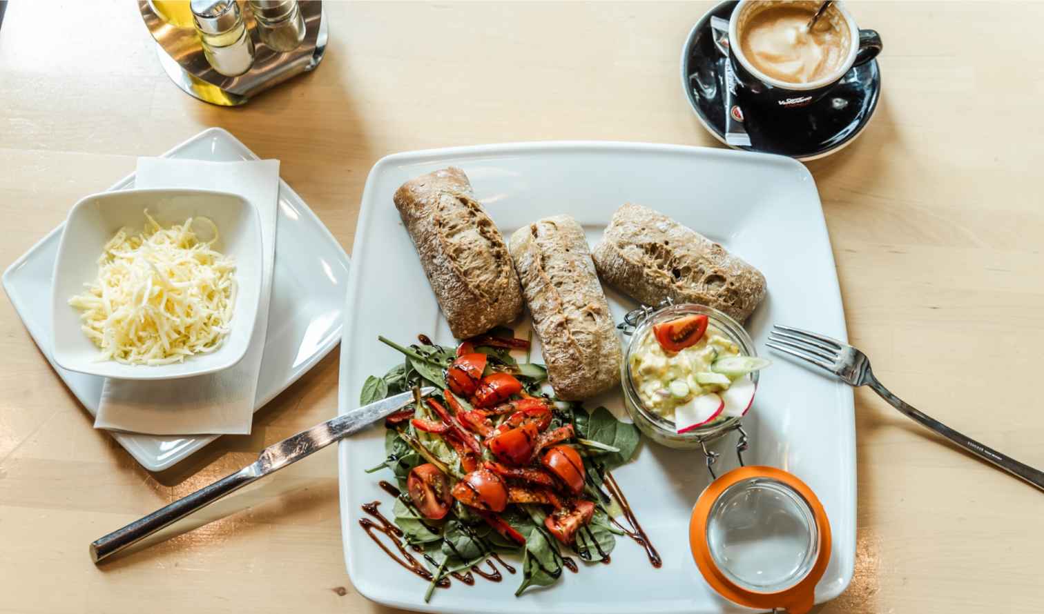 Plate with ciabatta rolls, salad, and jar of yogurt dip on a wooden table in Budapest.