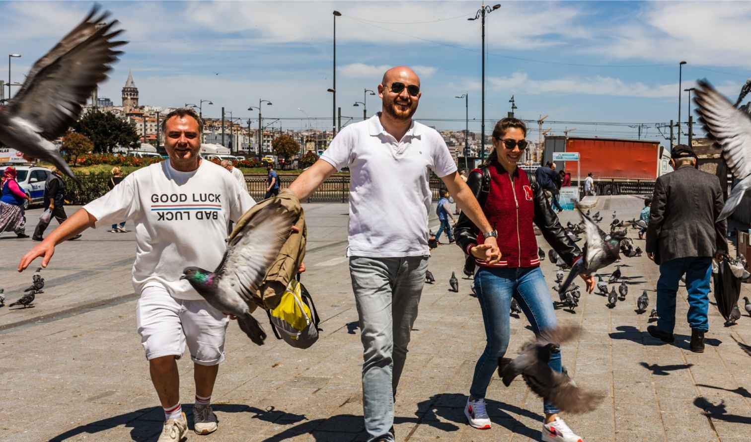 Pigeons flying around people in Taksim Square, Istanbul, with Galata Tower visible.