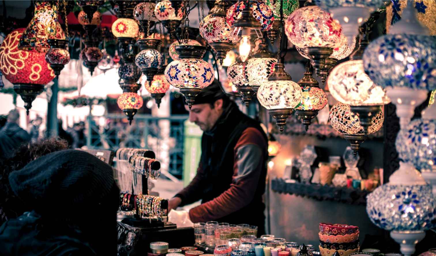 Vendor arranging lamps and bracelets at a market stall in Istanbul.