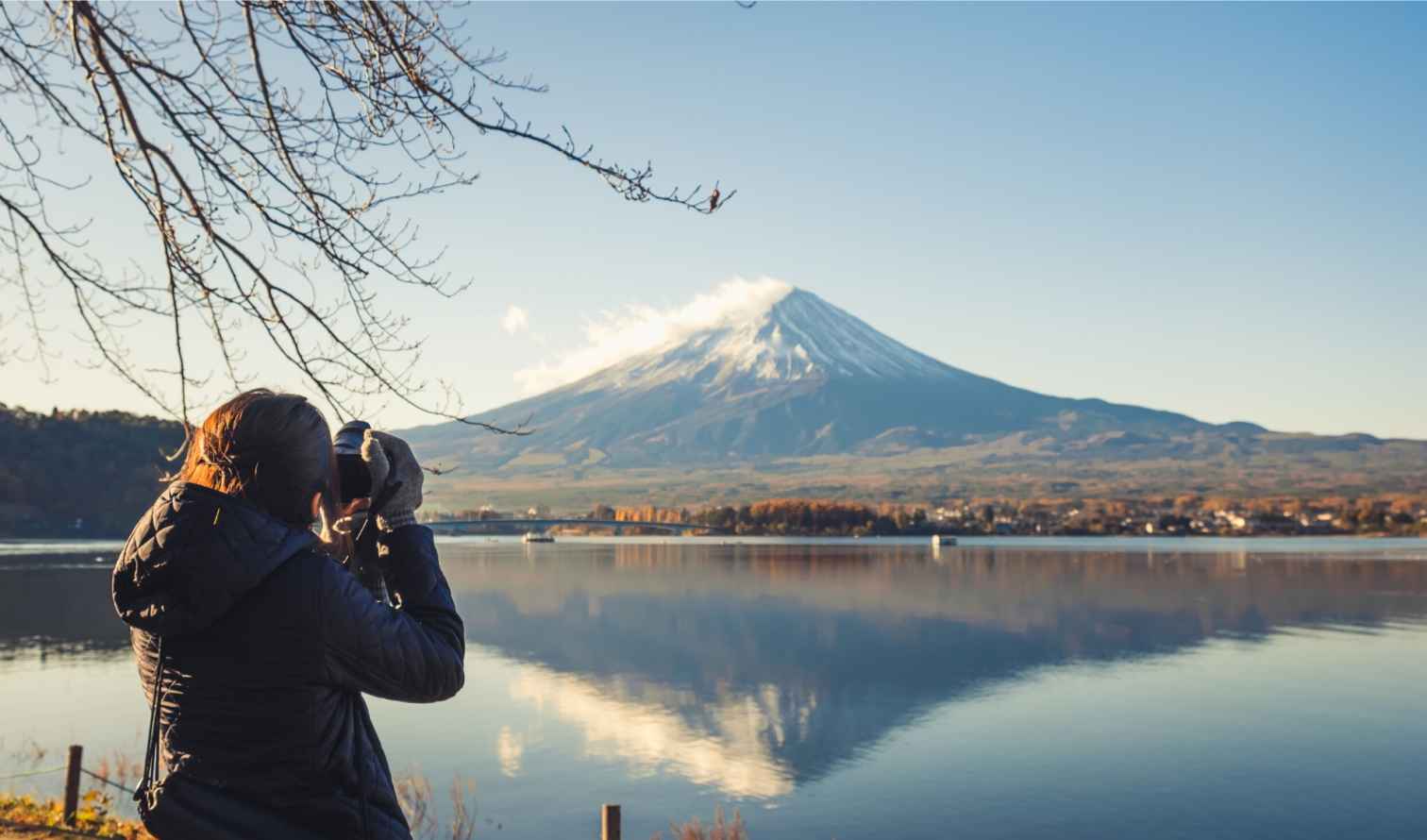 Mount Fuji with snow cap seen from across Lake Kawaguchi as person takes a photo.