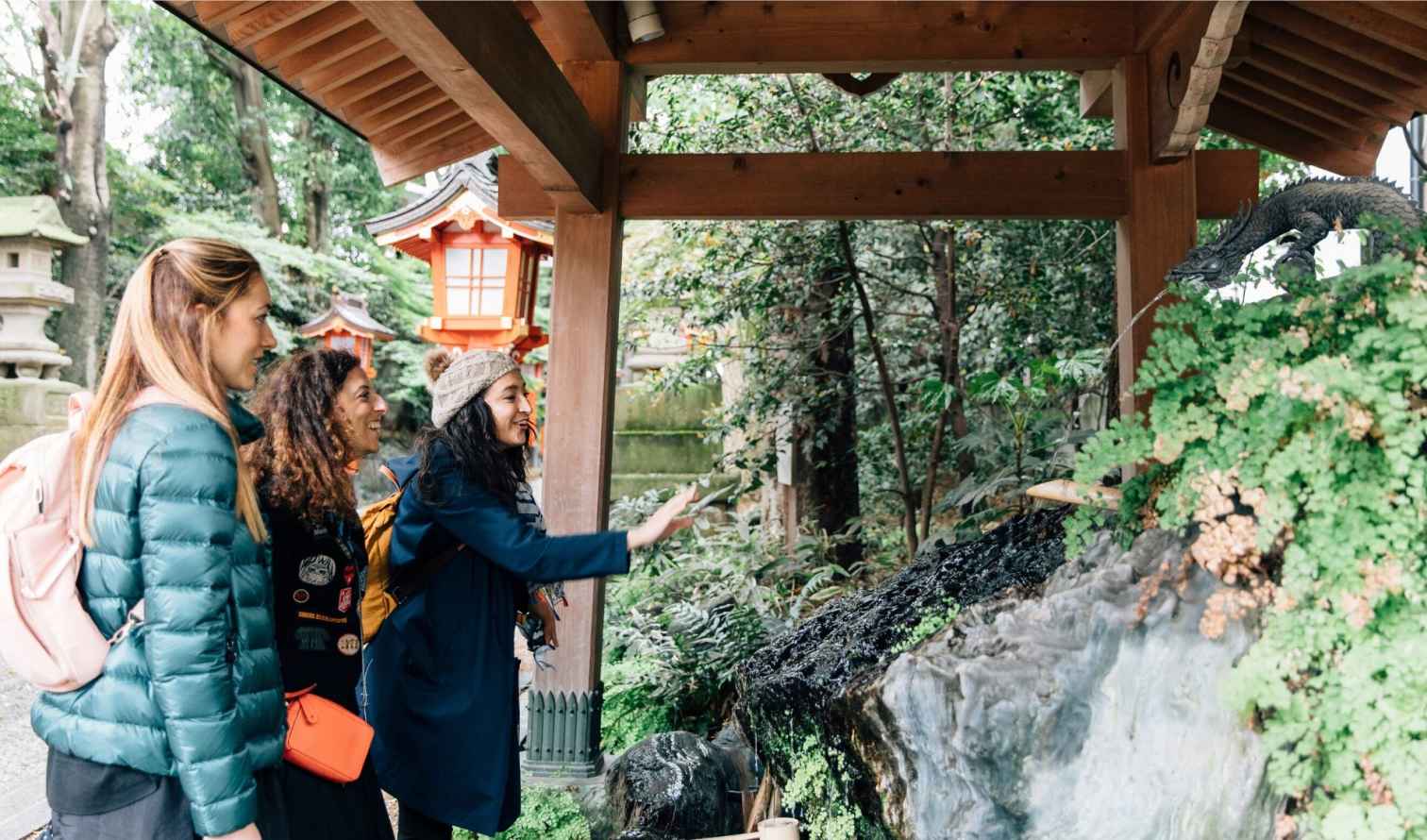 Three people visiting a shrine with a traditional water basin in Tokyo