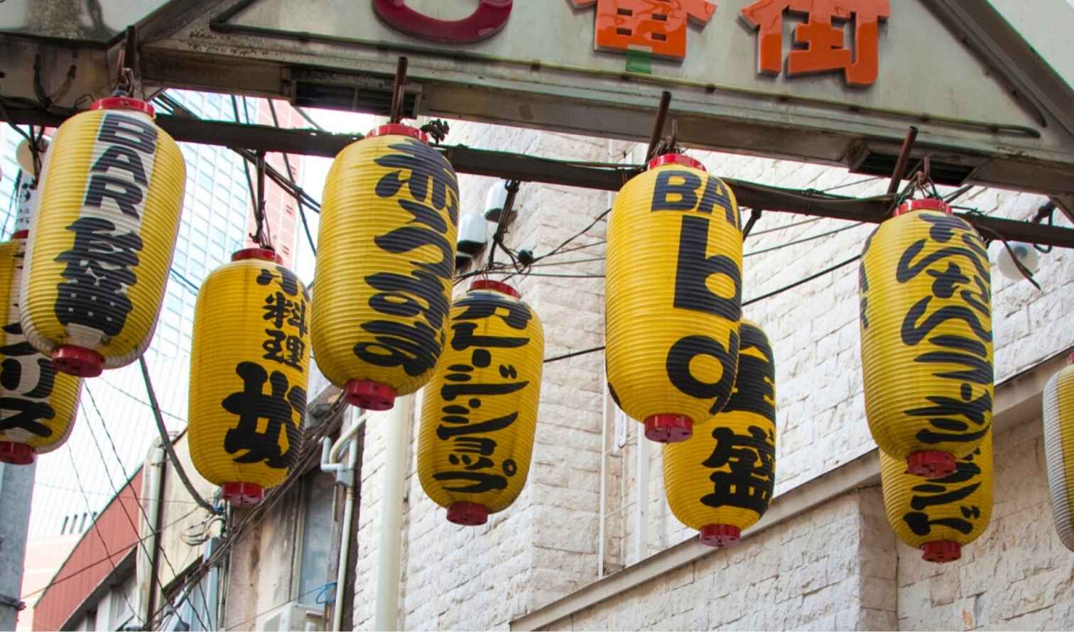 Yellow lanterns with Japanese writing hang above a street in Tokyo, Japan.