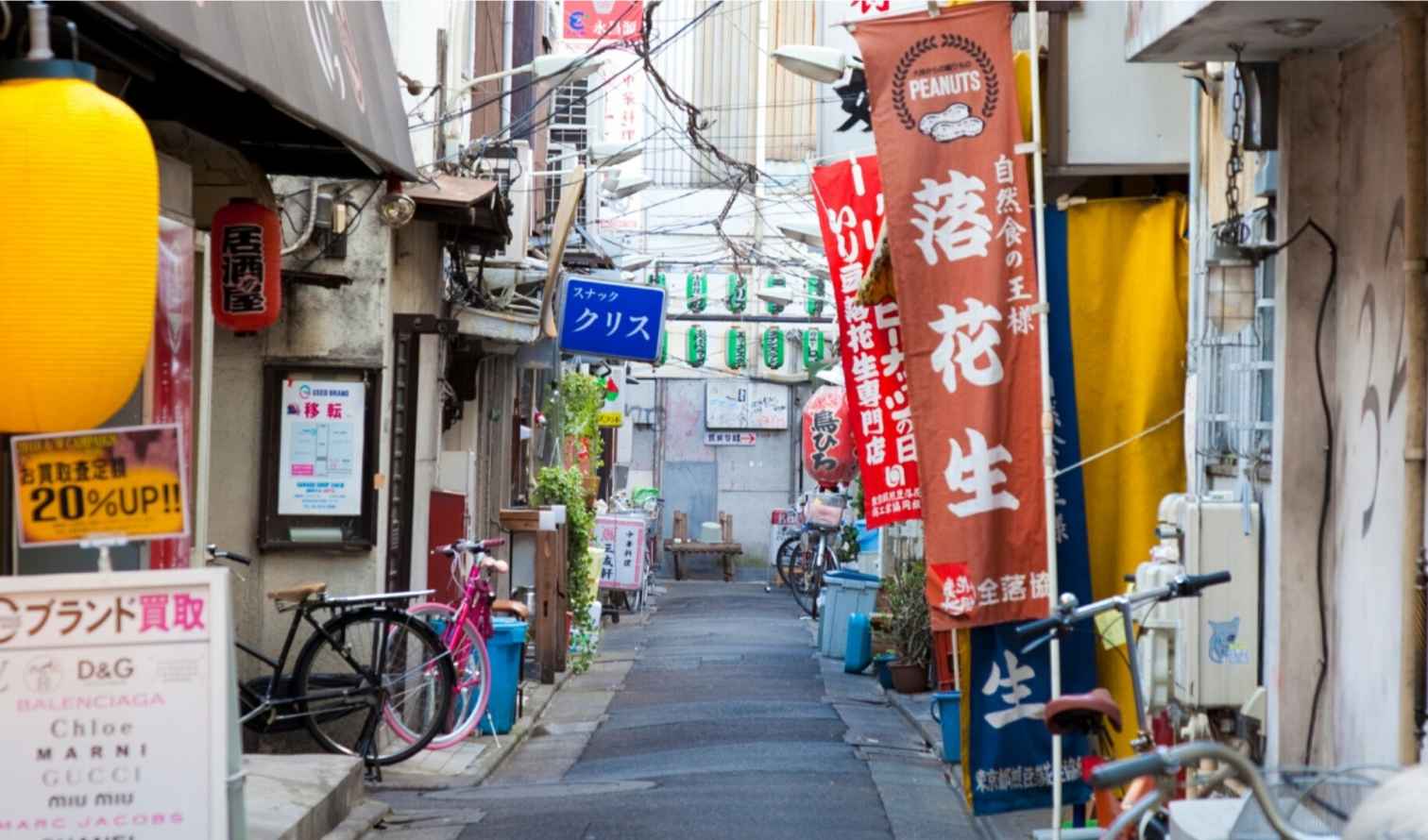 Narrow alleyway in Tokyo lined with colorful banners and bicycles.