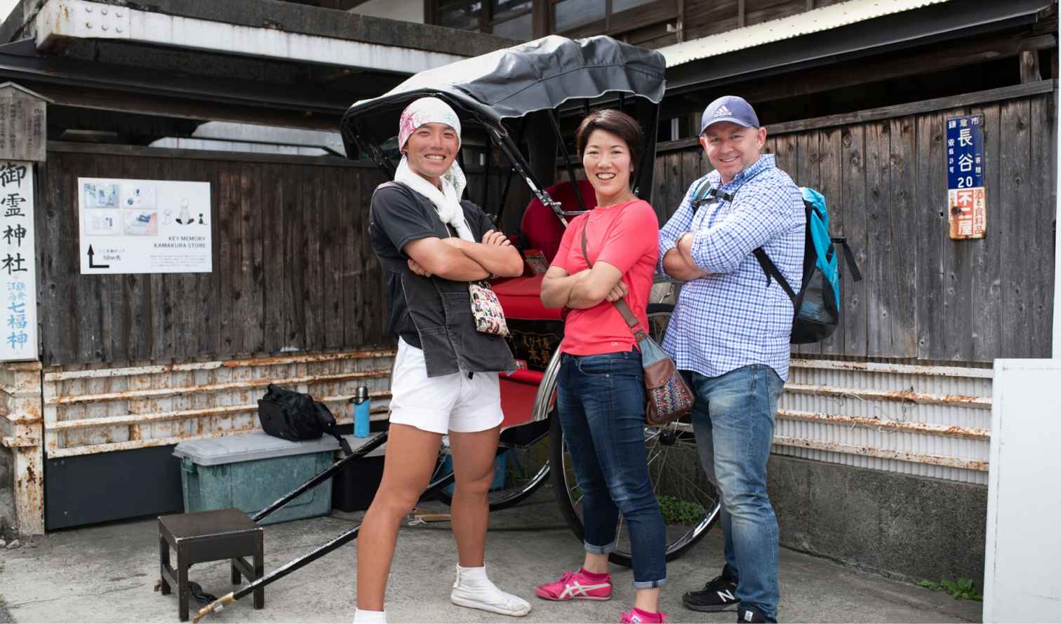 Three people standing in front of a rickshaw in Kamakura, Japan.
