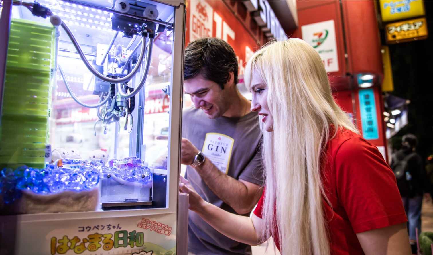 A man and a woman play a claw game in Tokyo arcade.