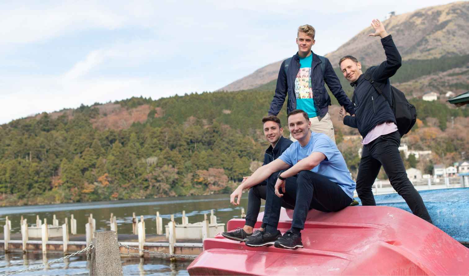 Group of four men sitting on red and blue boats by Lake Ashi, Japan.