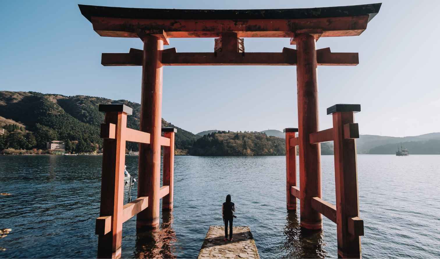 Person standing at Hakone Shrine's torii gate overlooking Lake Ashi.