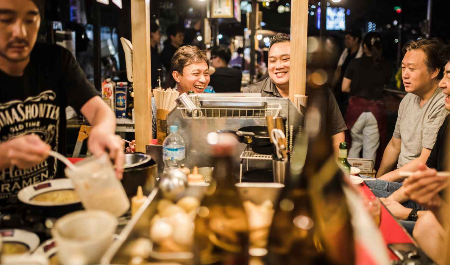 People sitting at a busy street food stall in Japan at night in Fukuoka
