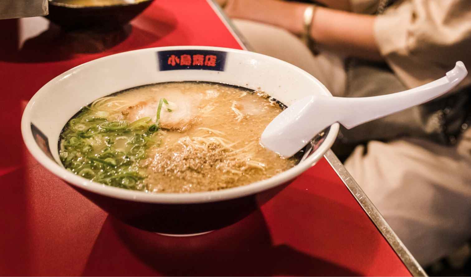 Bowl of ramen with green onions and pork on a red table in Fukuoka