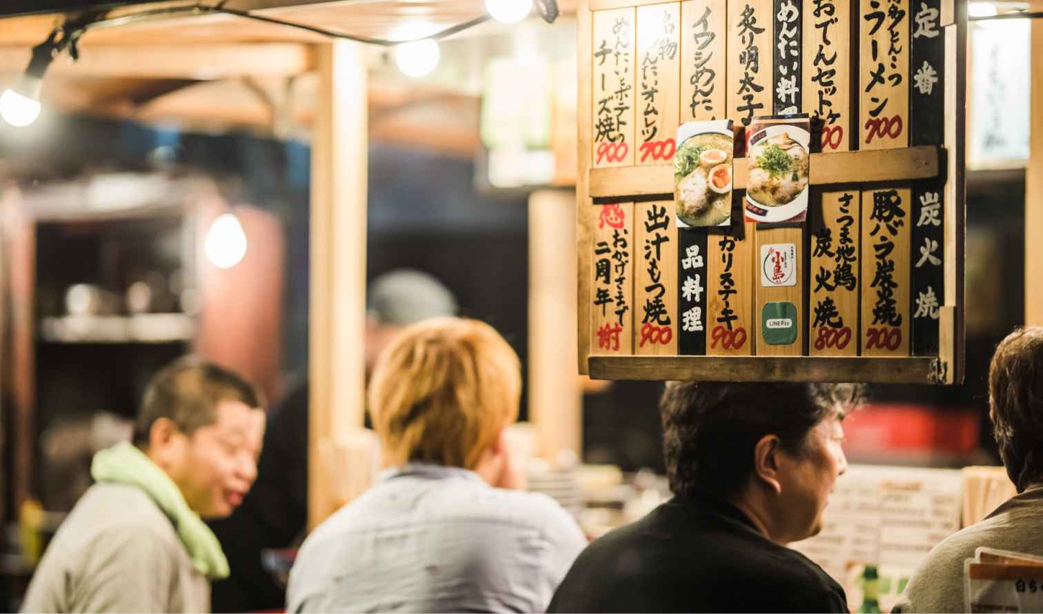 Diners sit at a Japanese street food stall with a menu on display in Fukuoka
