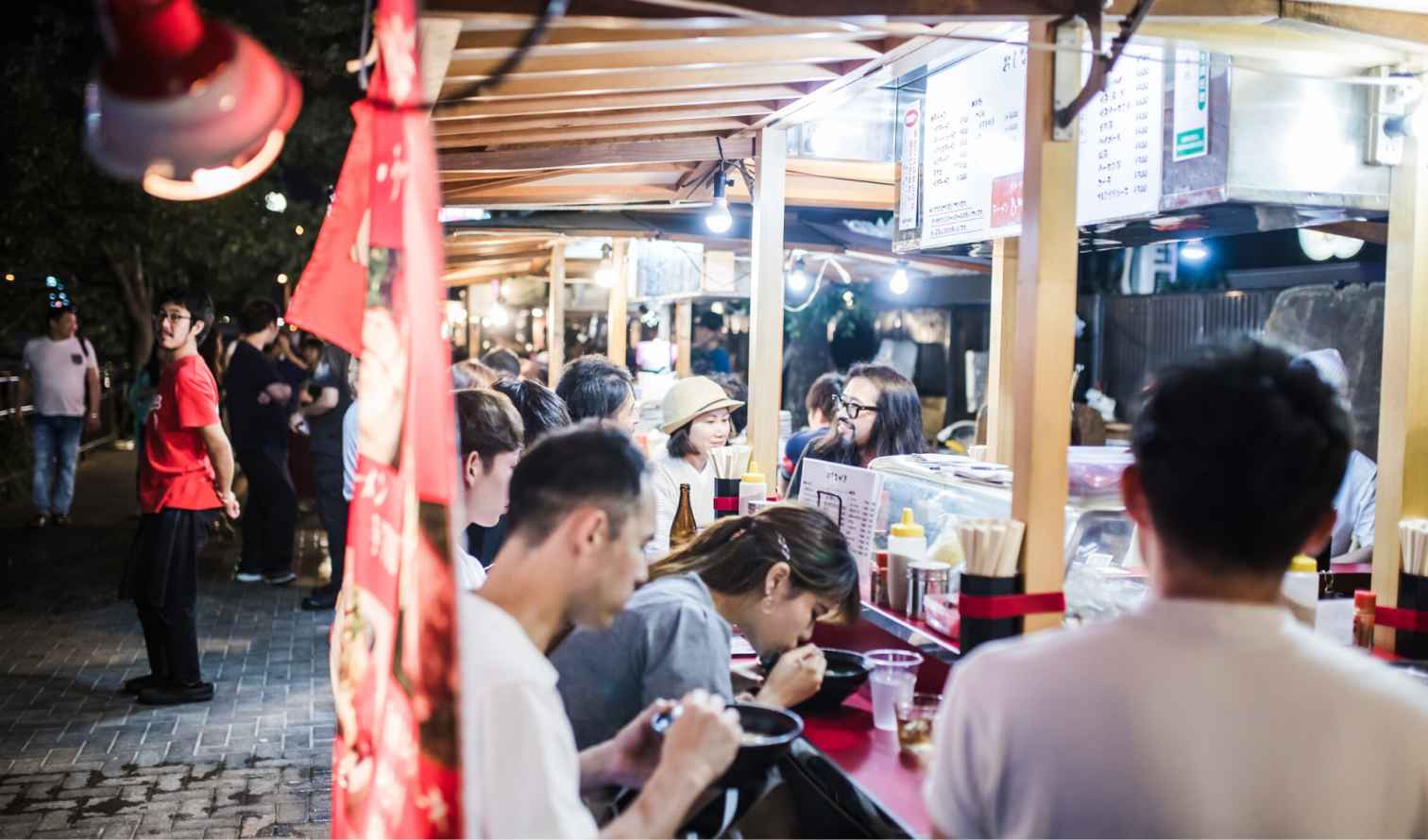 People eating at a street food stall, possibly in a Japanese urban area in Fukuoka