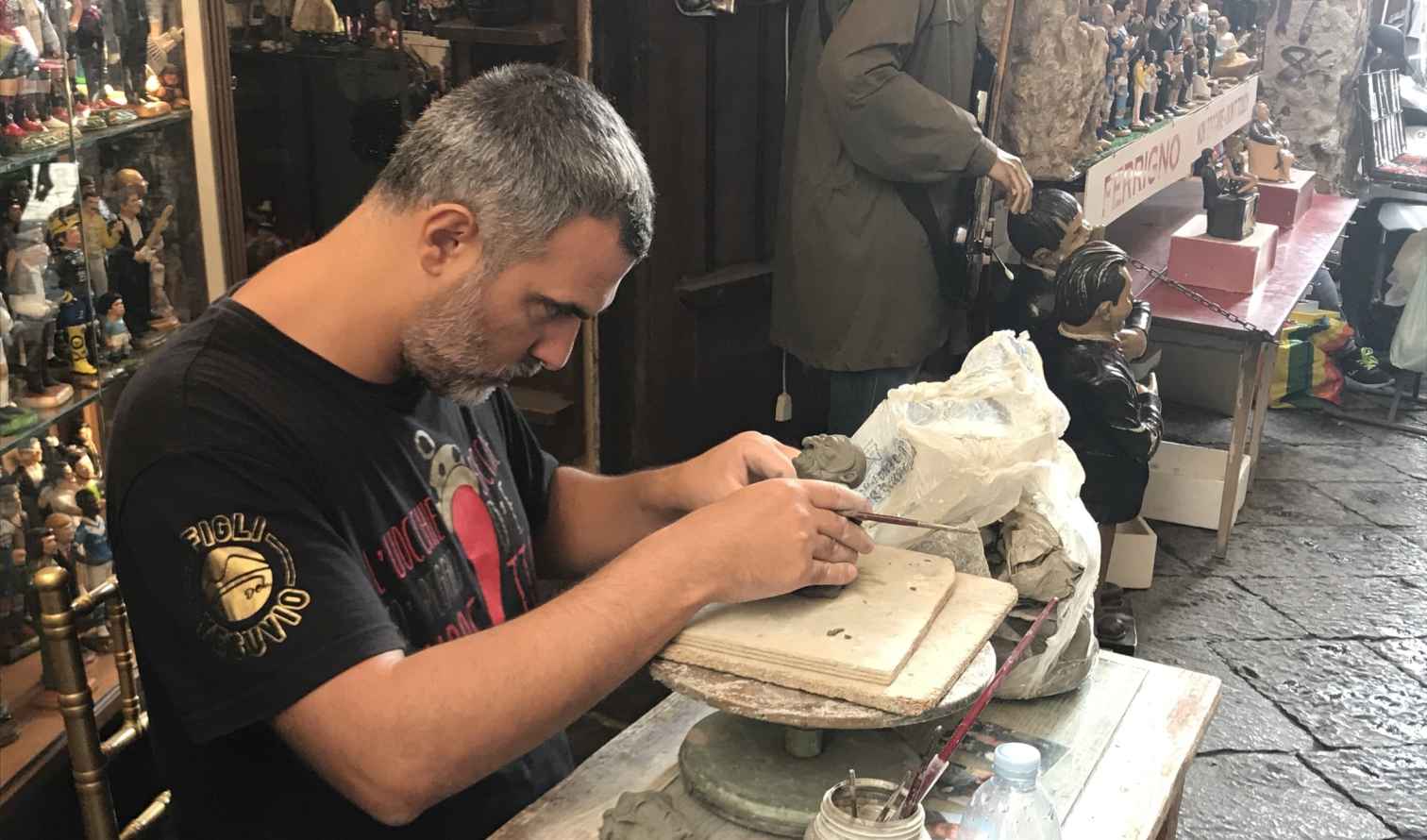 Man sculpting clay figures on a table in Naples workshop.