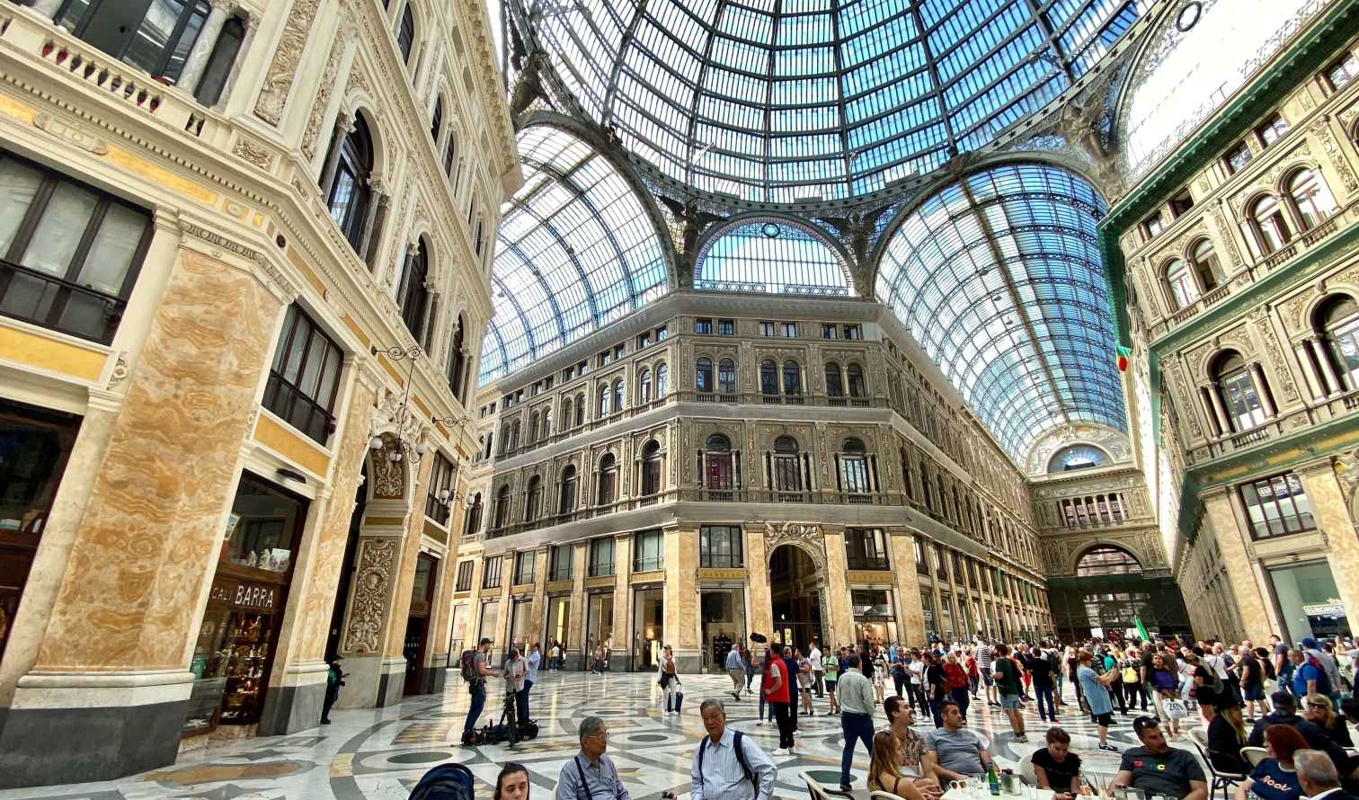 People dining beneath the glass dome of Galleria Umberto I in Naples.