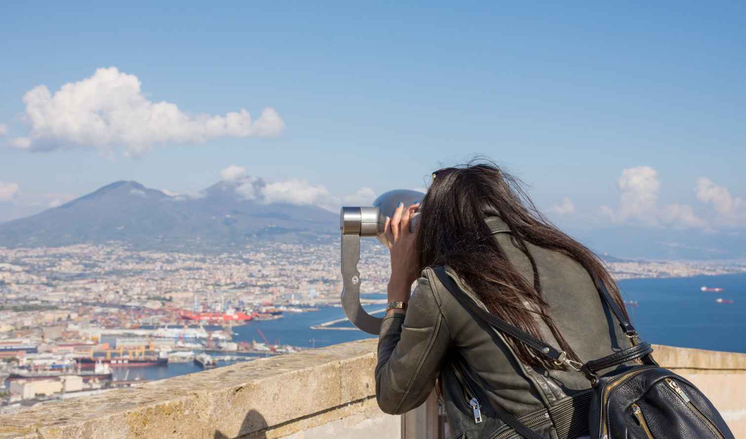 Person viewing Naples from a telescope with Mount Vesuvius in the background.