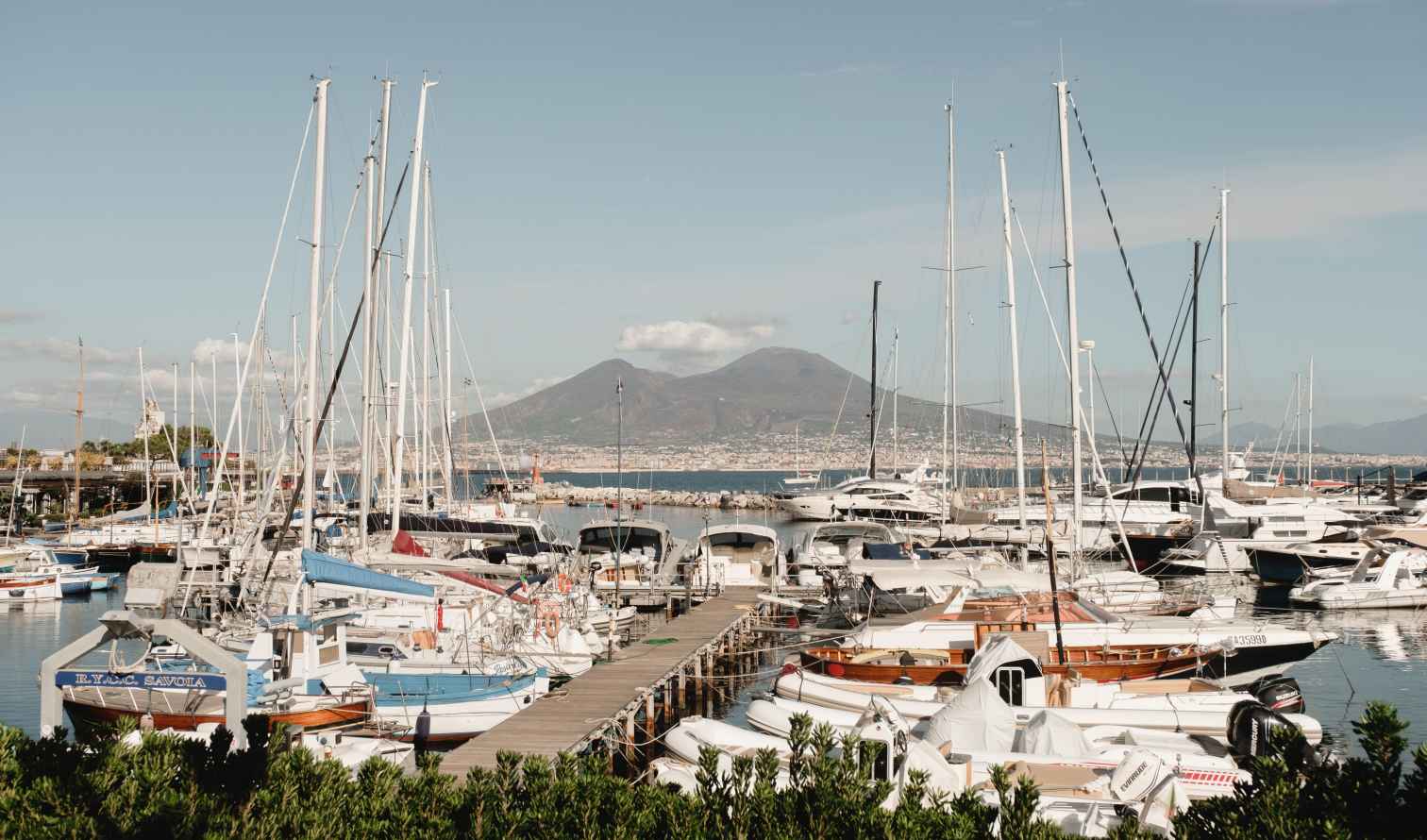 Boats docked at a marina with Mount Vesuvius in the background.