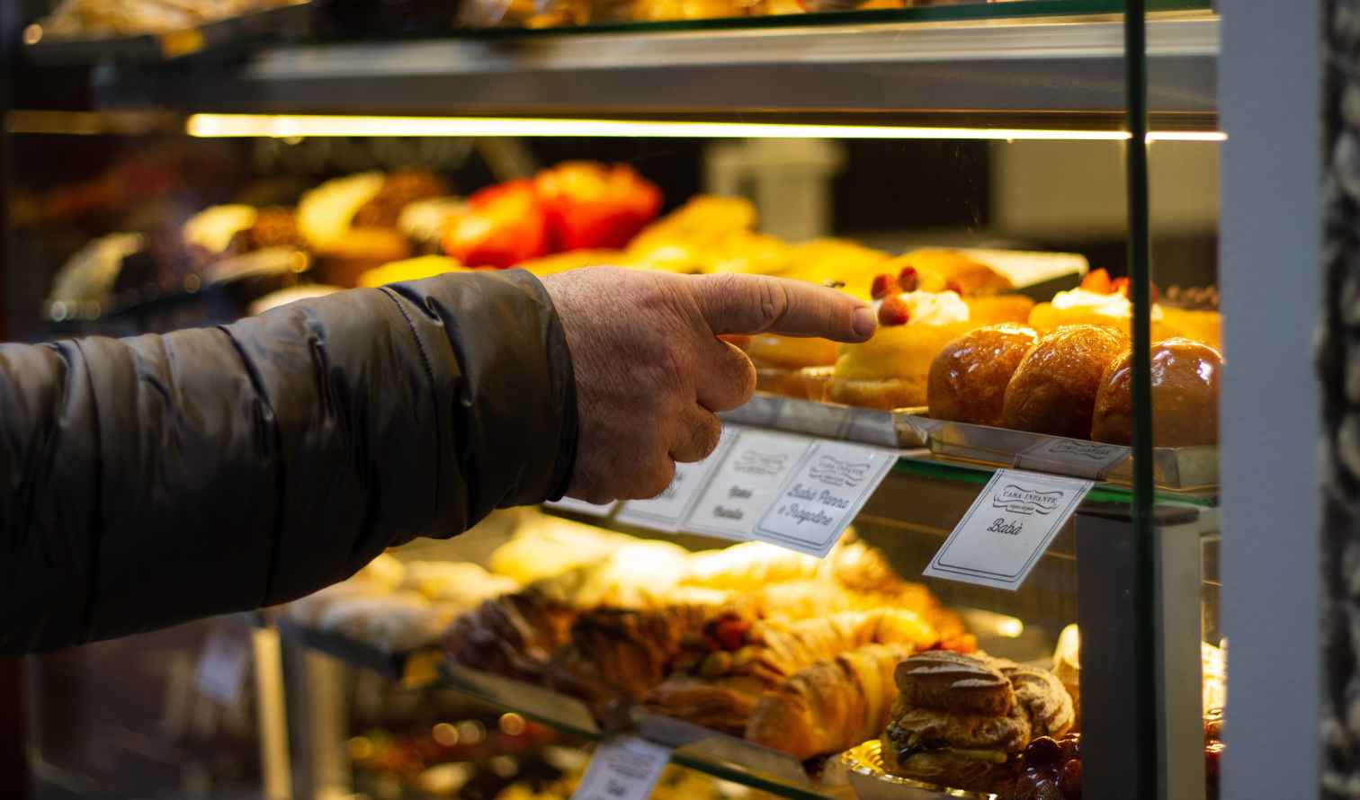 Person pointing at pastries in a bakery display in Naples