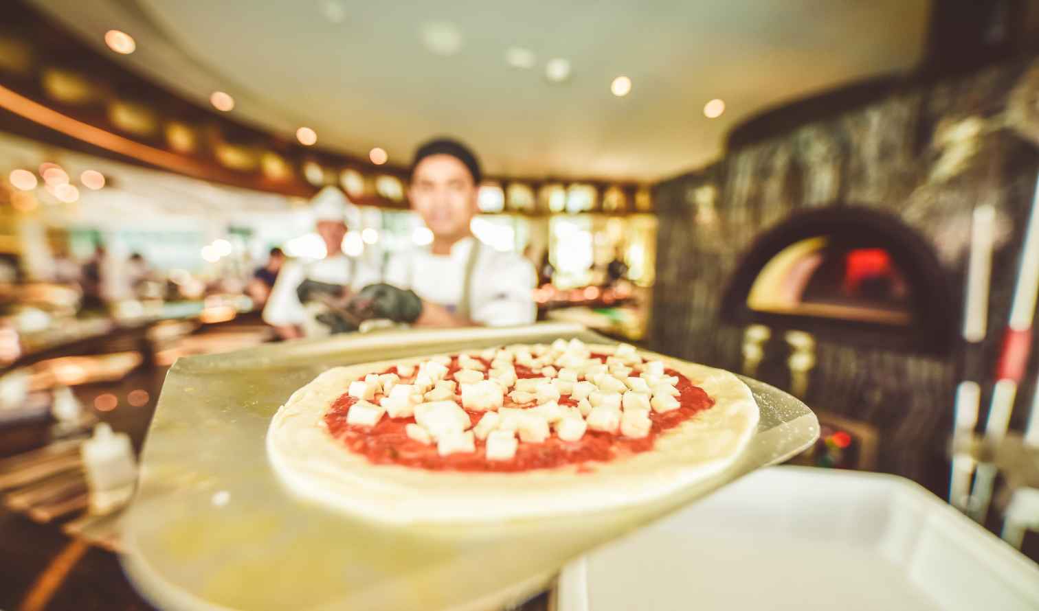 Chef prepares pizza with cheese and tomato sauce in a restaurant kitchen in Naples