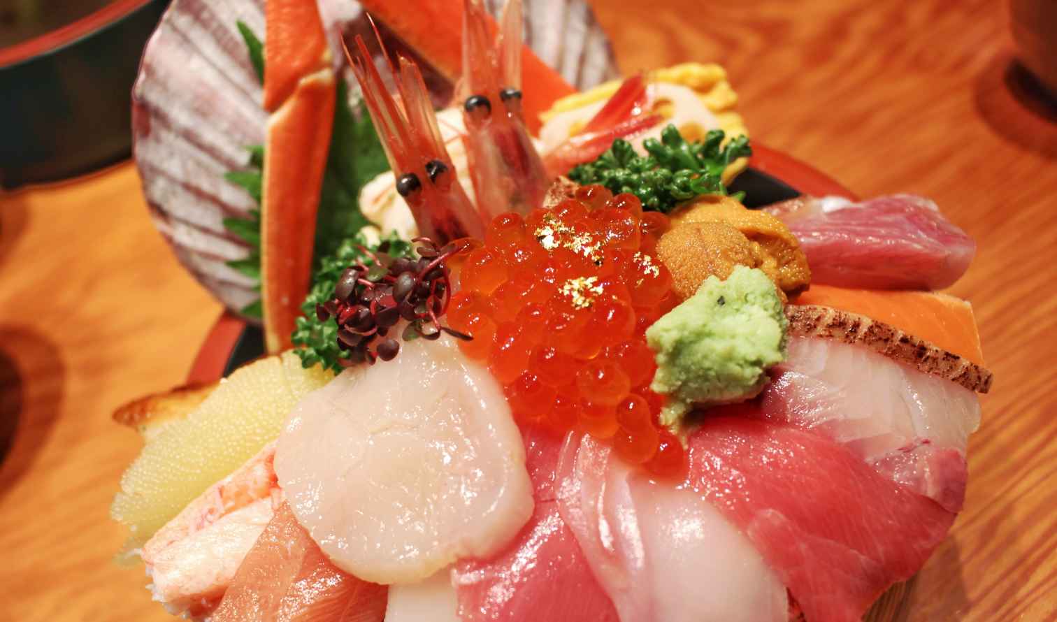 Donburi bowl featuring ikura, prawns, fish, and wasabi on a wooden surface in Kanazawa