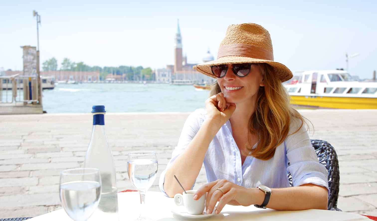 Woman sitting at a waterfront cafe in Venice, Italy with boats in the background.