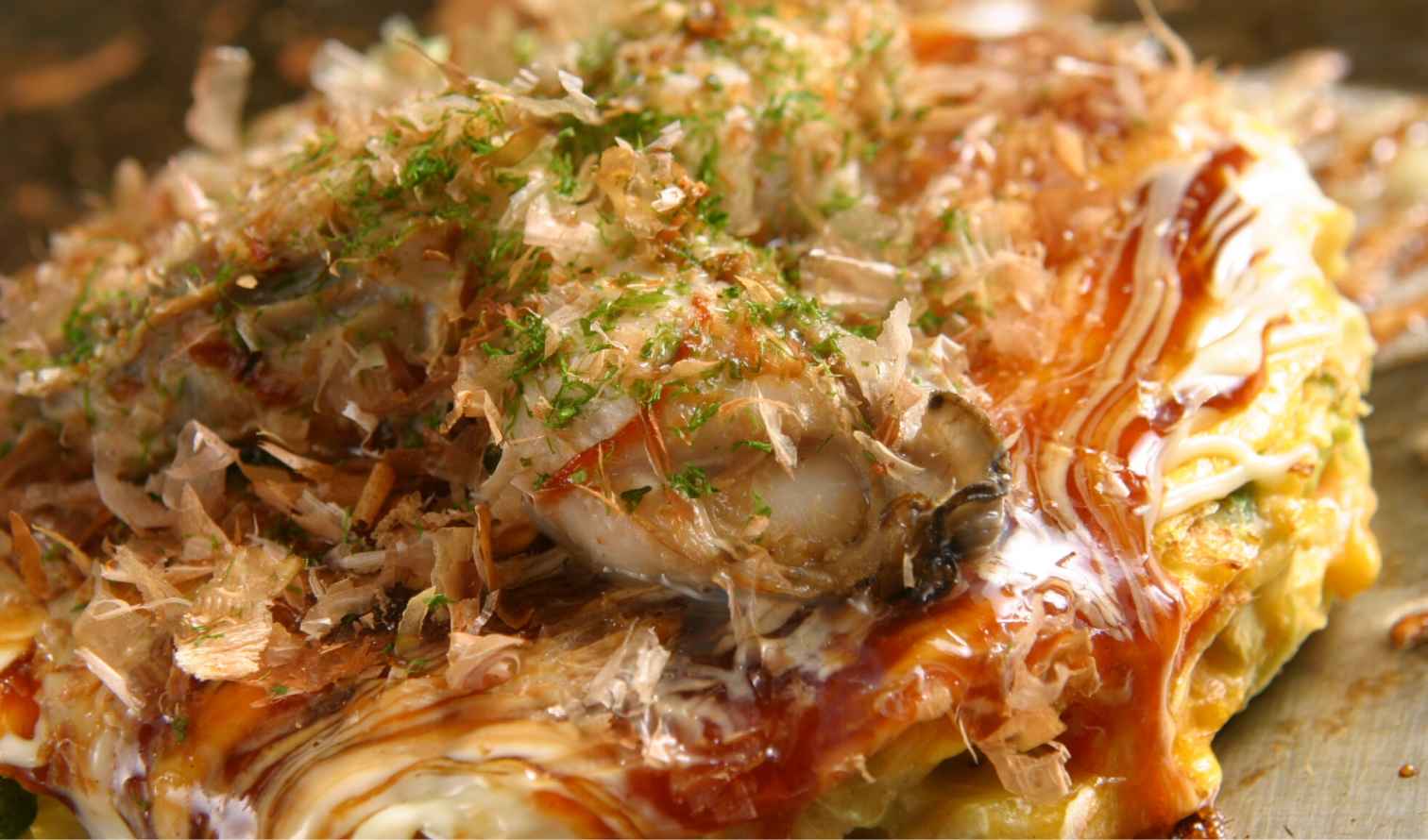 Close-up of a cooked okonomiyaki with seafood and bonito flakes on top in Osaka