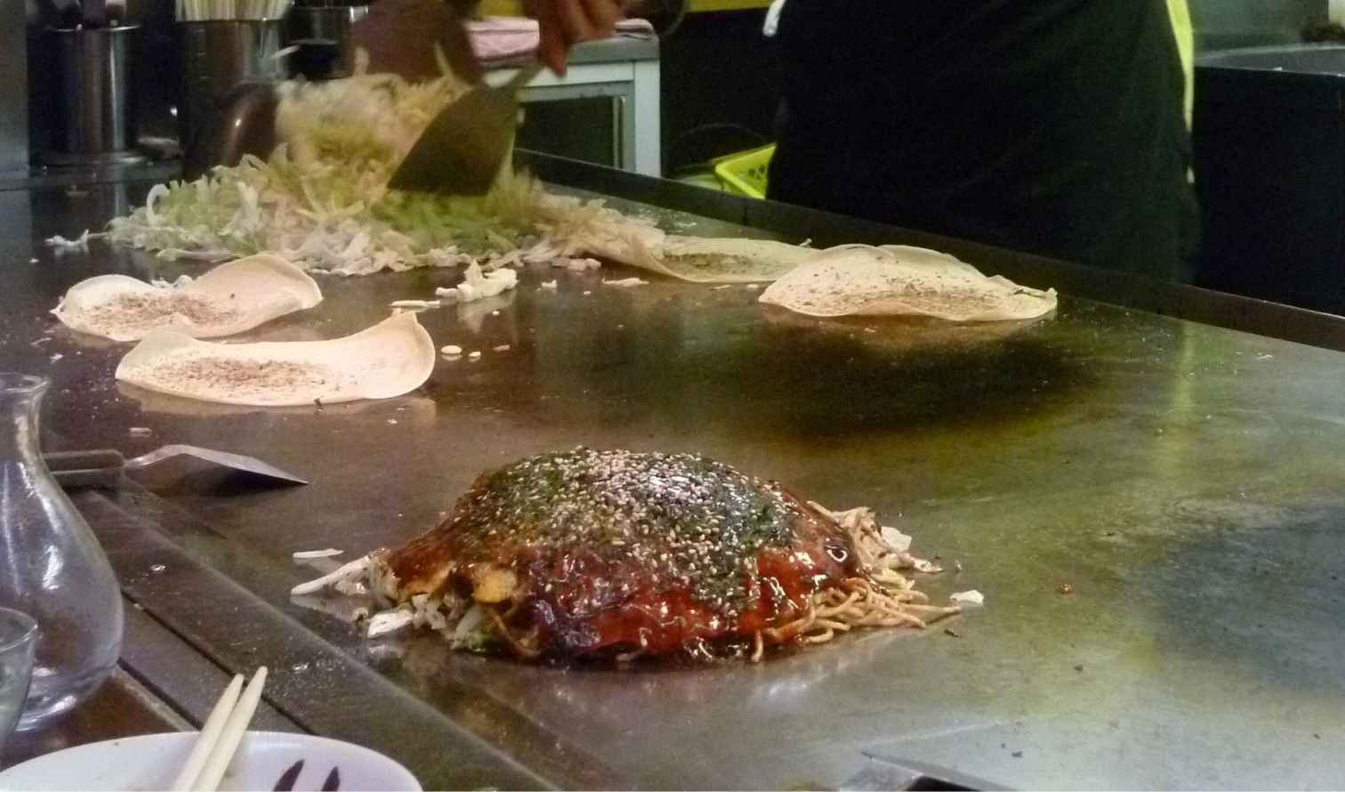 Okonomiyaki being prepared on a hot plate in a Japanese restaurant in Osaka