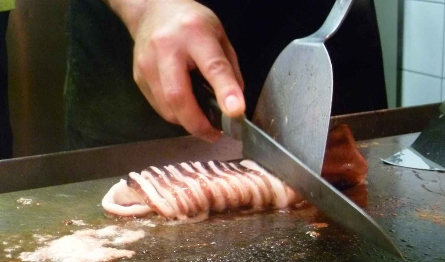 Chef slicing grilled squid on a teppanyaki grill in Hiroshima