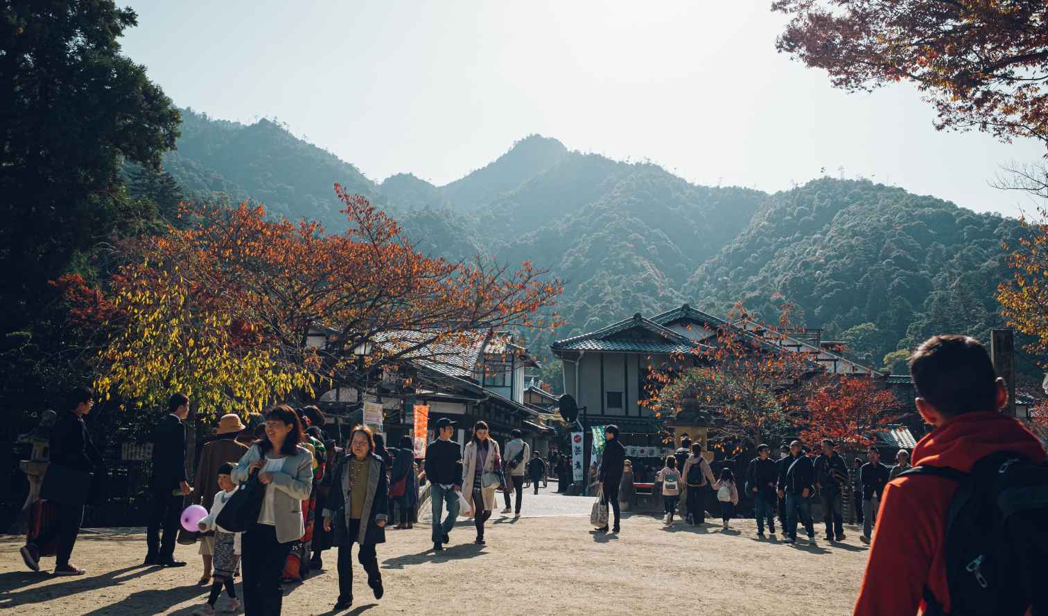 People walking near traditional Japanese buildings at a scenic mountain backdrop in Hiroshima