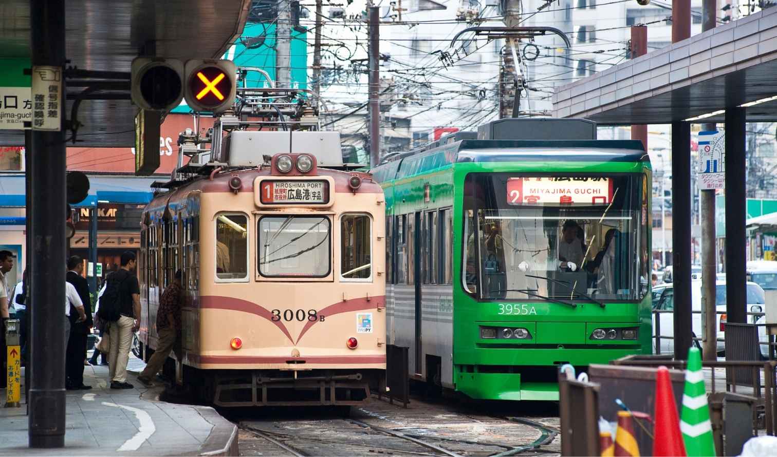 Trams at a station in Hiroshima, Japan, with passengers boarding.