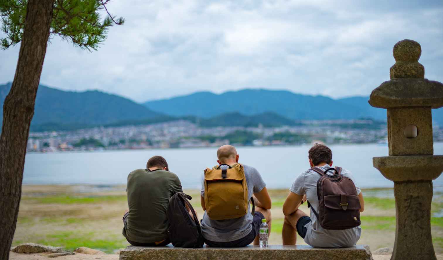 Three people sit on a ledge facing Hiroshima Bay in Japan.