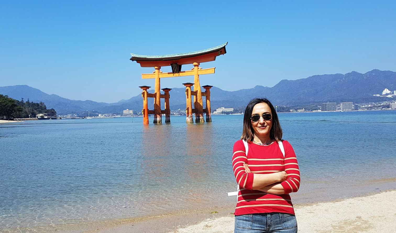 A person stands in front of the Itsukushima Shrine's floating torii gate in Hiroshima